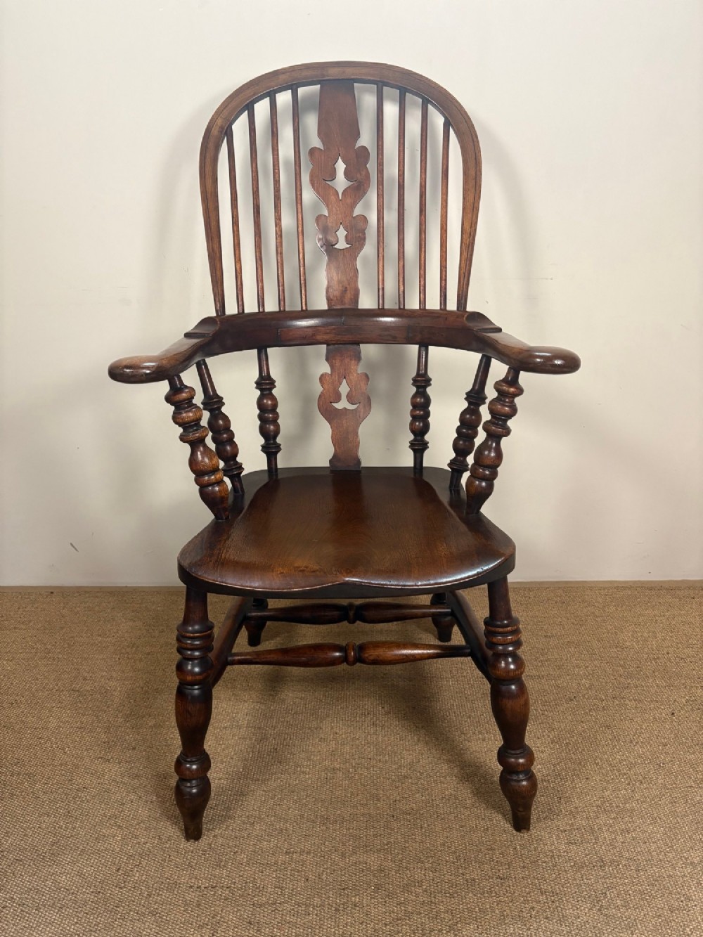 A nineteenth-century elm and beech Windsor armchair featuring a high hoop back, pierced central splat, turned spindles, curved armrests, and turned legs linked by an H-stretcher. View II