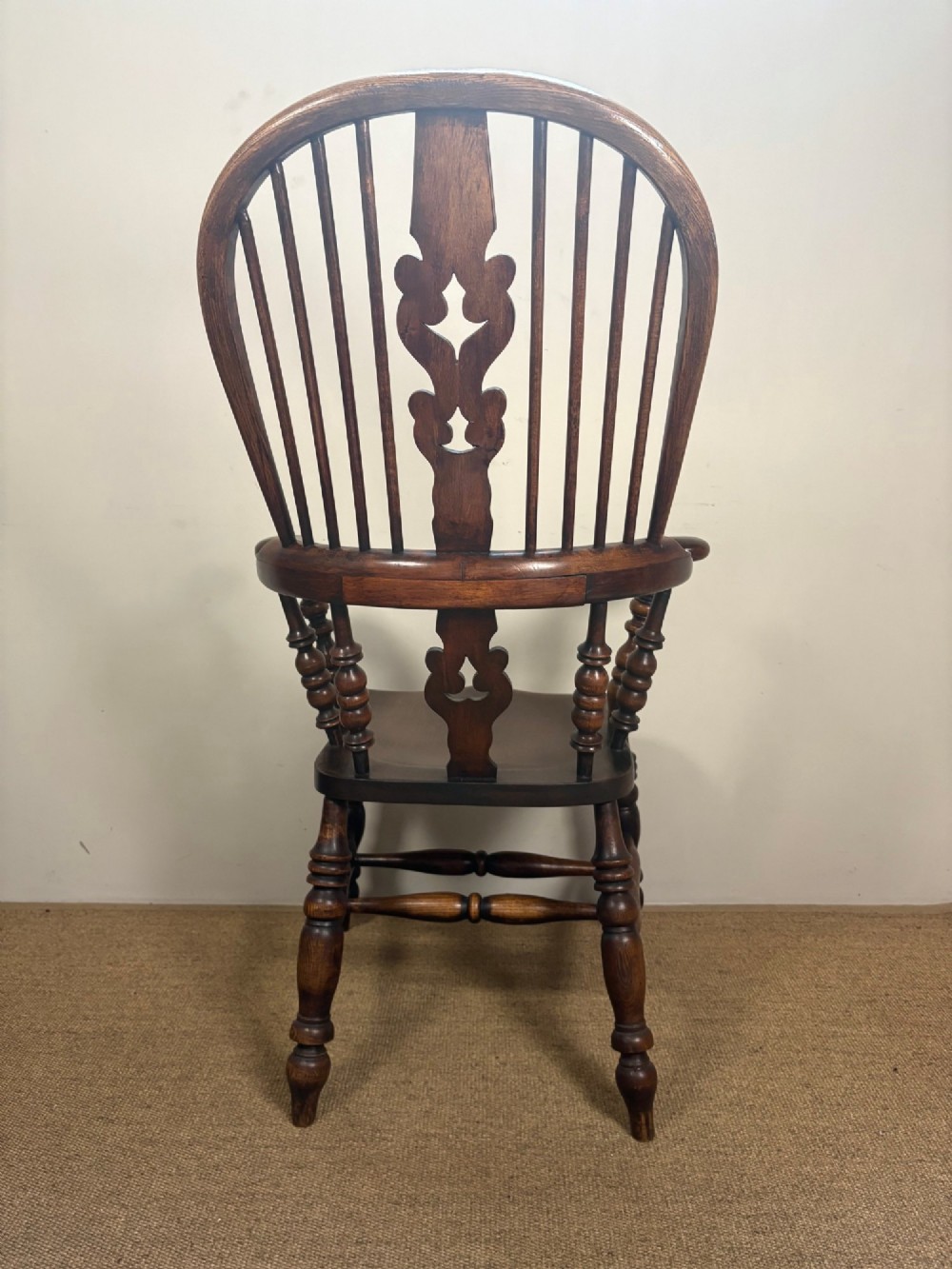 A nineteenth-century elm and beech Windsor armchair featuring a high hoop back, pierced central splat, turned spindles, curved armrests, and turned legs linked by an H-stretcher. View IV