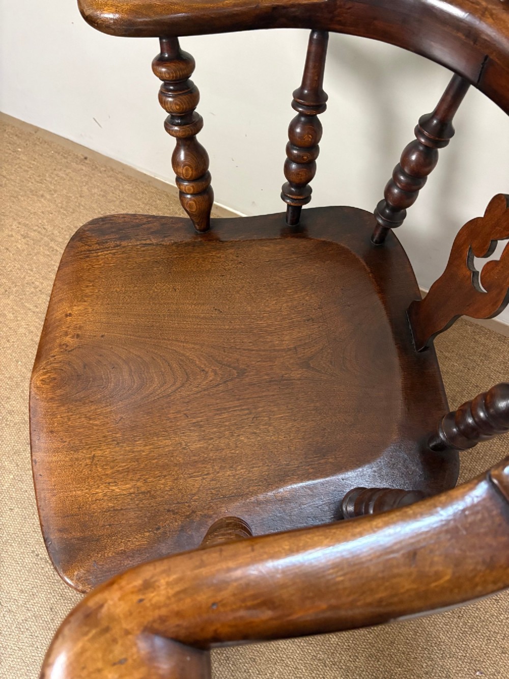 A nineteenth-century elm and beech Windsor armchair featuring a high hoop back, pierced central splat, turned spindles, curved armrests, and turned legs linked by an H-stretcher. View V