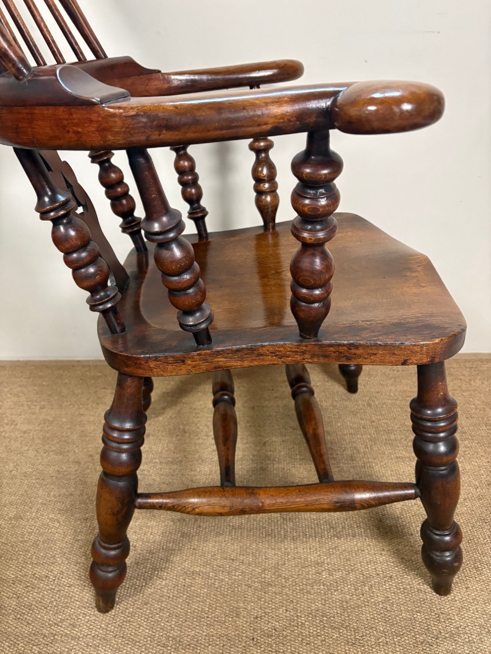 A nineteenth-century elm and beech Windsor armchair featuring a high hoop back, pierced central splat, turned spindles, curved armrests, and turned legs linked by an H-stretcher. View VI