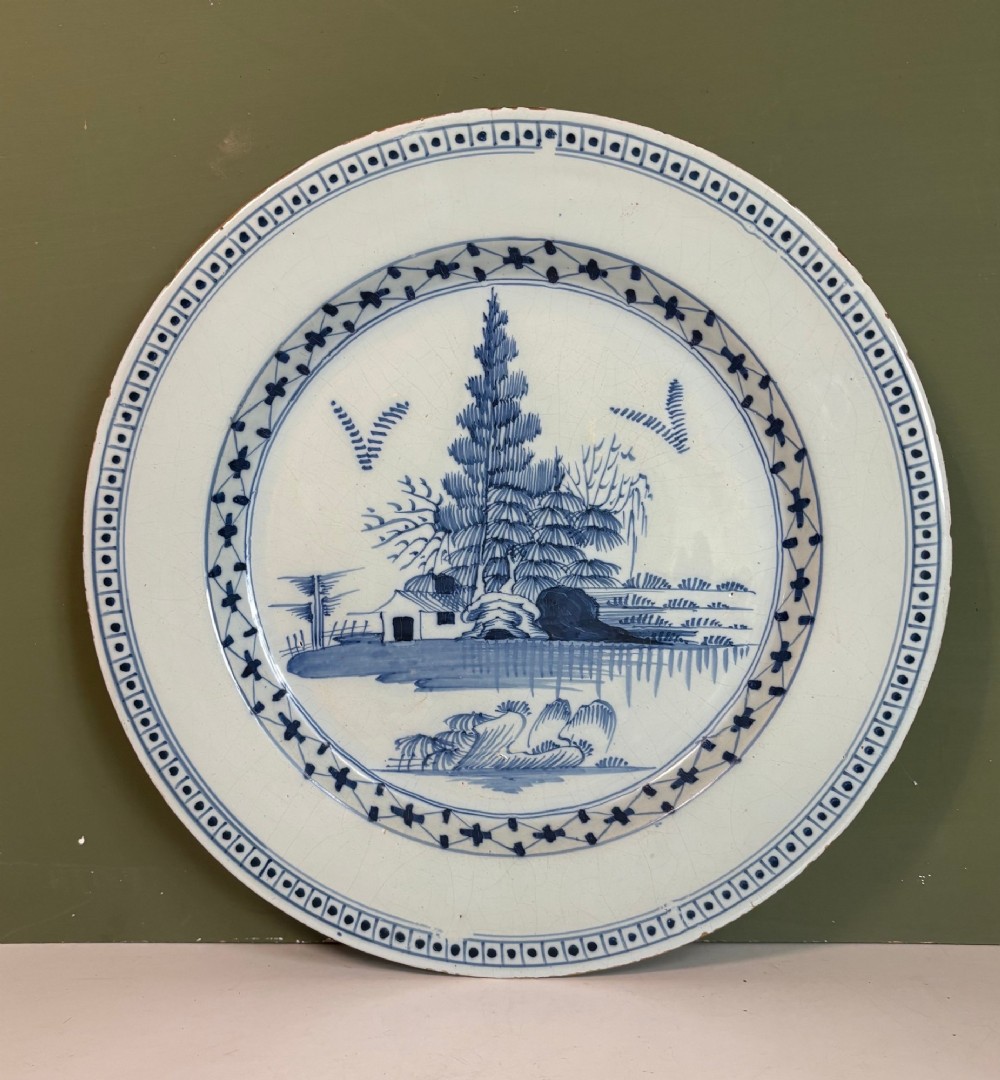 An 18th-century circular tin-glazed earthenware charger featuring hand-painted cobalt blue trees and geometric borders on a white ground.