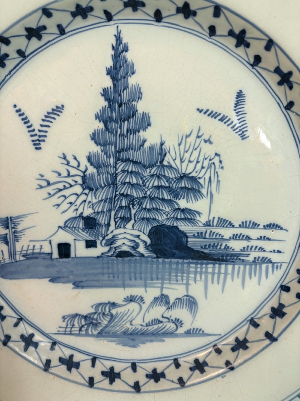 An 18th-century circular tin-glazed earthenware charger featuring hand-painted cobalt blue trees and geometric borders on a white ground. View III