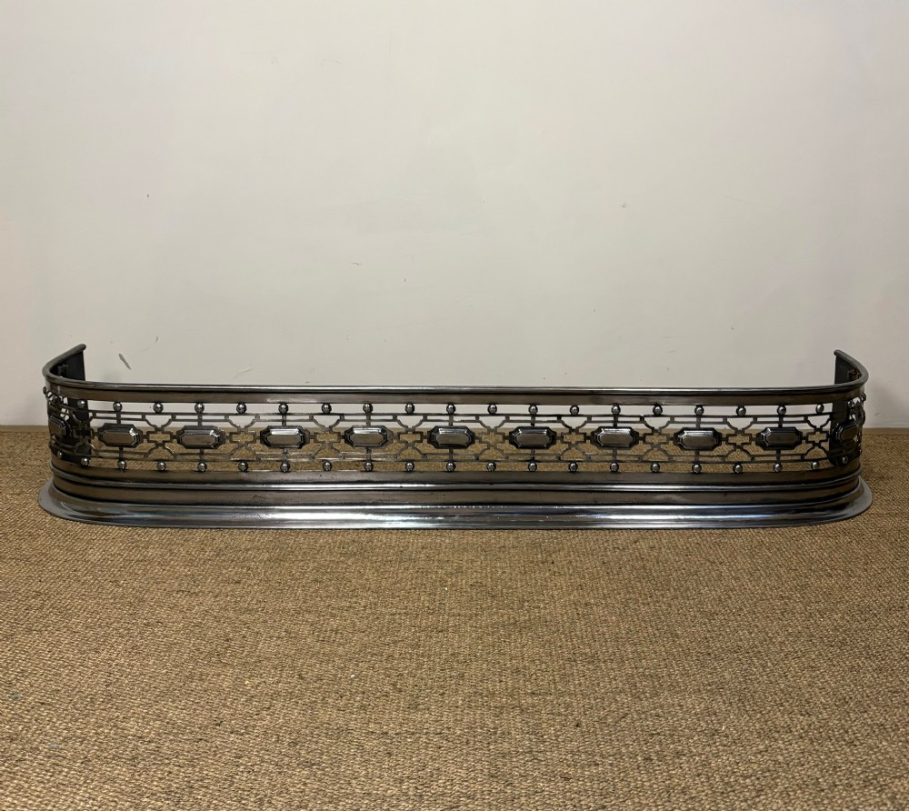 A nineteenth-century burnished steel fireplace fender featuring a curved front with geometric pierced fretwork and raised studs. View II