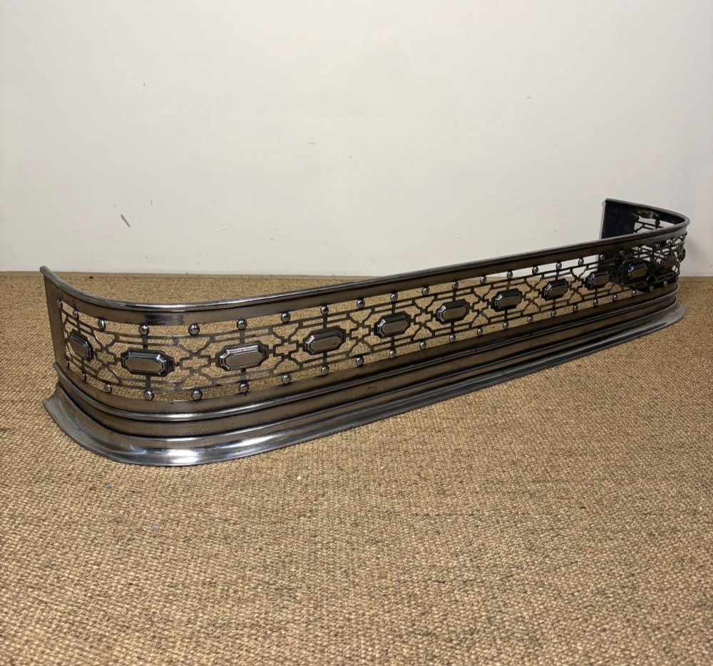 A nineteenth-century burnished steel fireplace fender featuring a curved front with geometric pierced fretwork and raised studs.