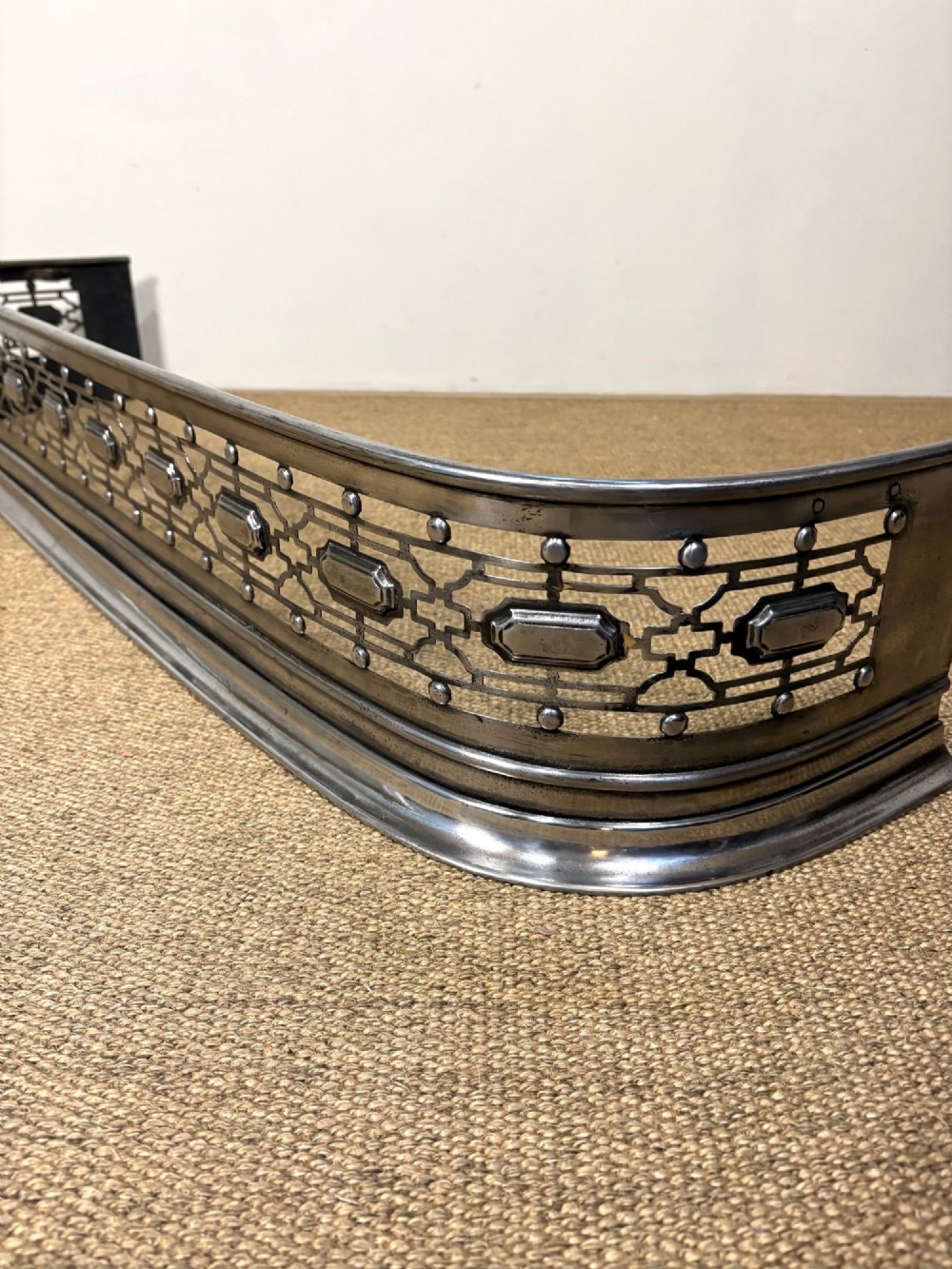 A nineteenth-century burnished steel fireplace fender featuring a curved front with geometric pierced fretwork and raised studs. View IV