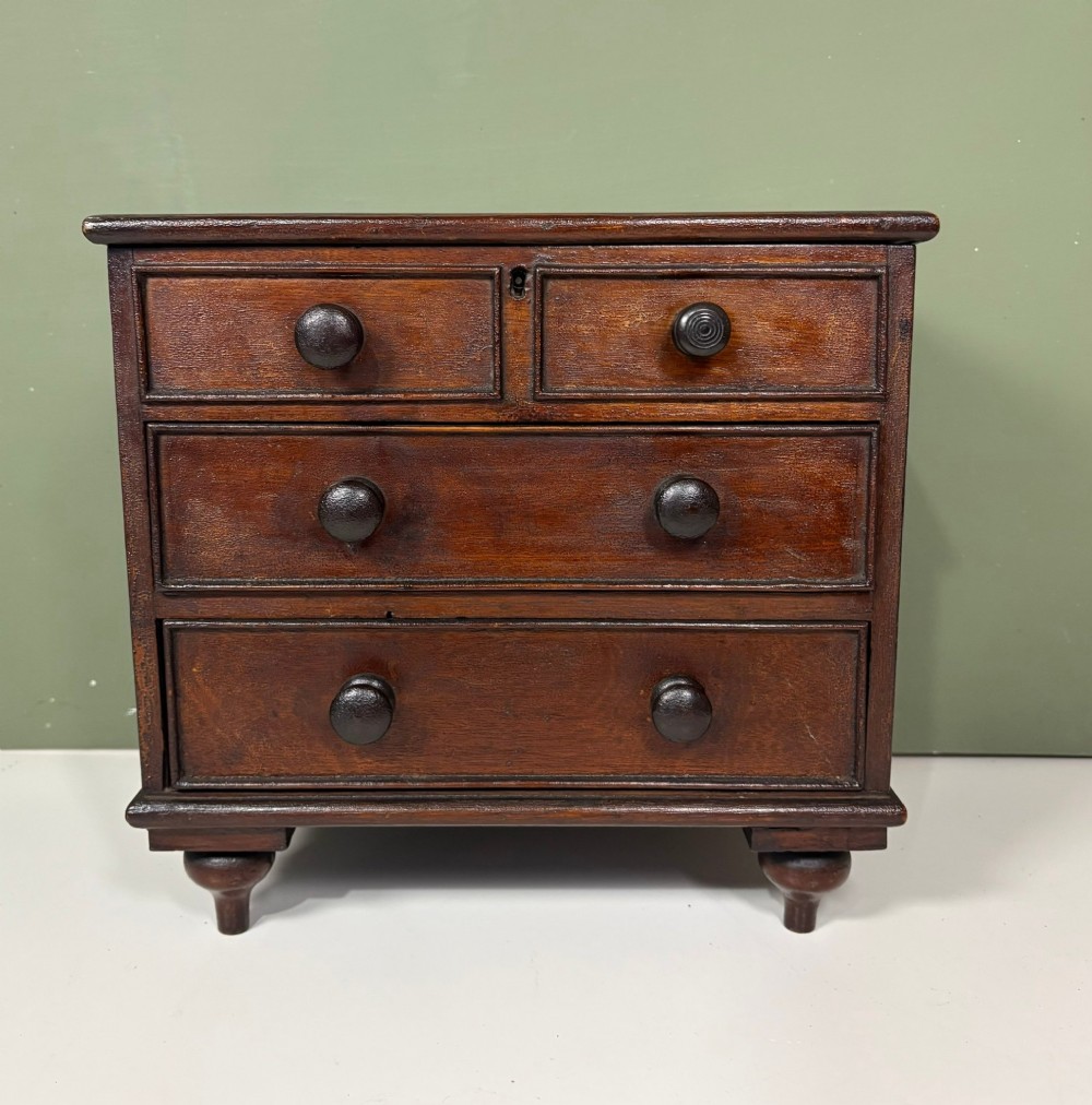 A 19th-century dark oak miniature chest featuring a hinged top lid opening to partitioned compartments filled with sea shells, above three drawers with turned wooden knobs. View III