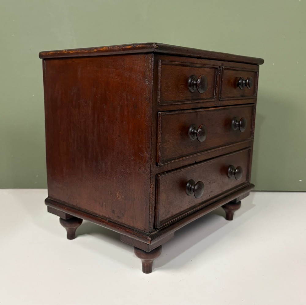 A 19th-century dark oak miniature chest featuring a hinged top lid opening to partitioned compartments filled with sea shells, above three drawers with turned wooden knobs. View IV