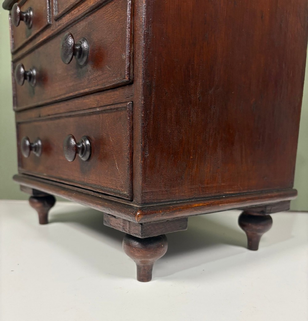 A 19th-century dark oak miniature chest featuring a hinged top lid opening to partitioned compartments filled with sea shells, above three drawers with turned wooden knobs. View V
