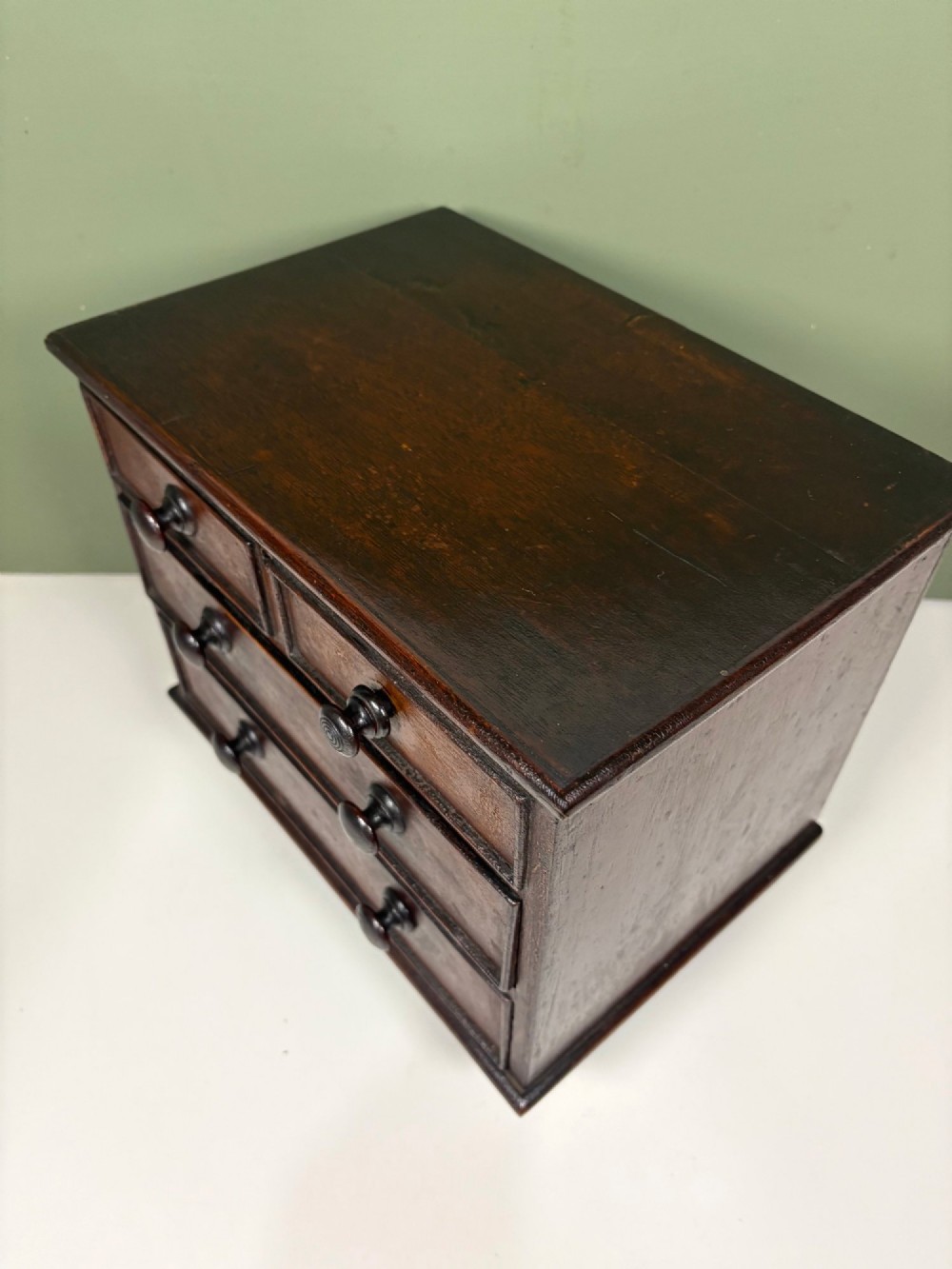 A 19th-century dark oak miniature chest featuring a hinged top lid opening to partitioned compartments filled with sea shells, above three drawers with turned wooden knobs. View VI