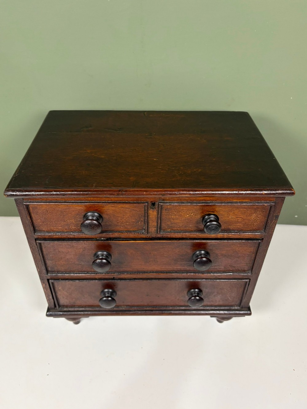 A 19th-century dark oak miniature chest featuring a hinged top lid opening to partitioned compartments filled with sea shells, above three drawers with turned wooden knobs. View VIII
