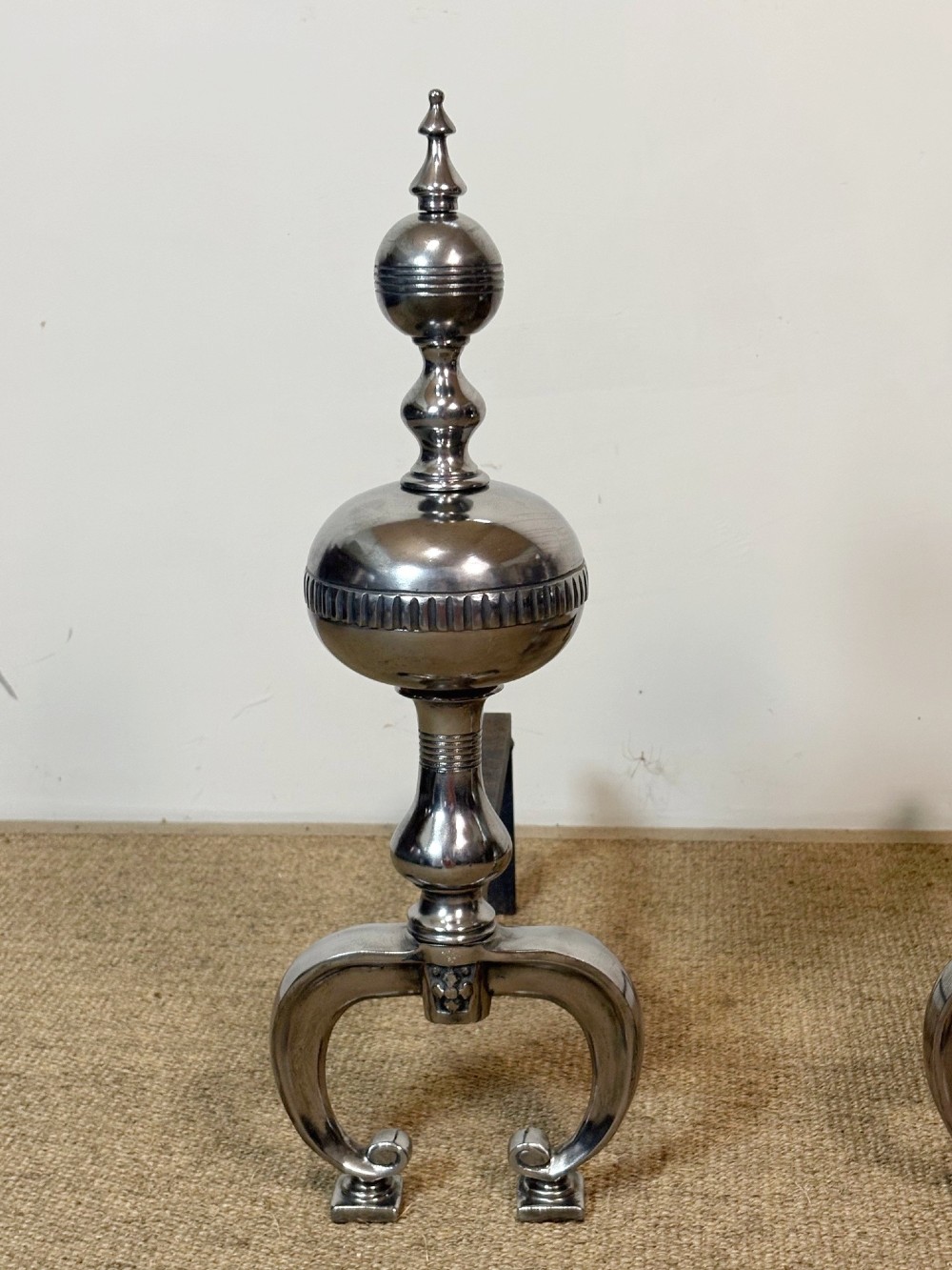 A pair of polished steel fire dogs featuring lathe-turned baluster columns, spherical fluted knops, topped with finials and supported on scrolled feet. View III