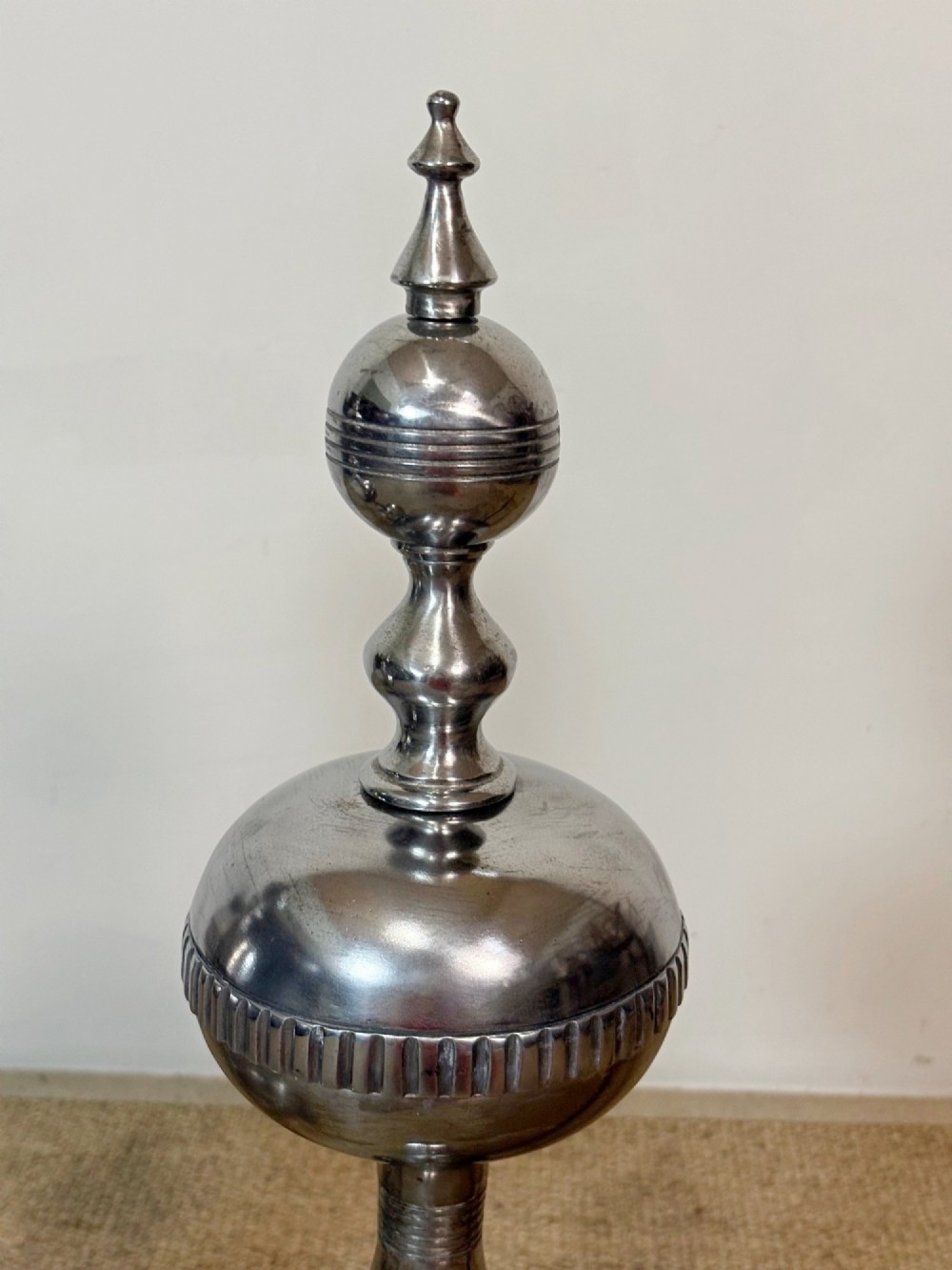 A pair of polished steel fire dogs featuring lathe-turned baluster columns, spherical fluted knops, topped with finials and supported on scrolled feet. View V