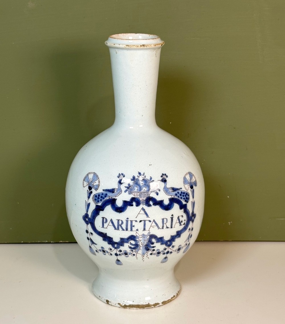 An 18th-century tin-glazed earthenware Delft apothecary bottle decorated with a hand-painted blue cartouche, peacocks, and Latin inscription.
