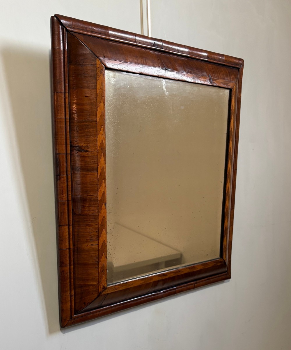 An 18th-century rectangular wall mirror featuring a cushion-moulded walnut frame with crossgrain veneers and herringbone inlay surrounding an aged reflective glass plate.