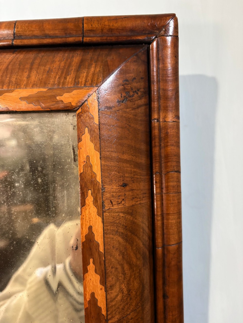 An 18th-century rectangular wall mirror featuring a cushion-moulded walnut frame with crossgrain veneers and herringbone inlay surrounding an aged reflective glass plate. View II