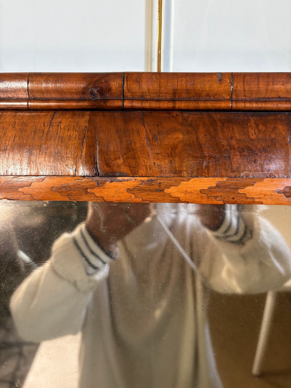 An 18th-century rectangular wall mirror featuring a cushion-moulded walnut frame with crossgrain veneers and herringbone inlay surrounding an aged reflective glass plate. View V