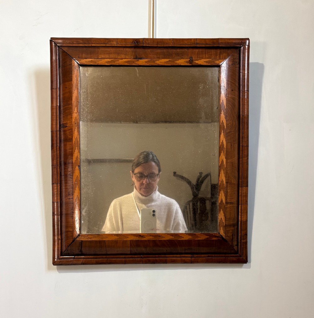 An 18th-century rectangular wall mirror featuring a cushion-moulded walnut frame with crossgrain veneers and herringbone inlay surrounding an aged reflective glass plate. View VI