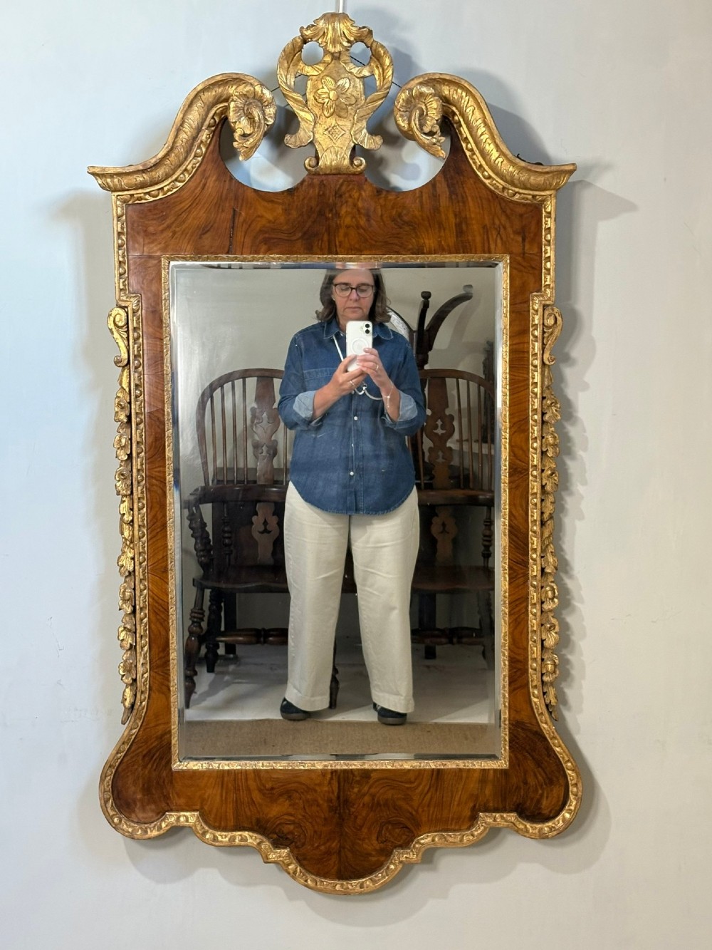 An eighteenth-century style wall mirror featuring a figured walnut veneer frame, carved giltwood foliate borders, a top cartouche cresting, and bevelled glass.