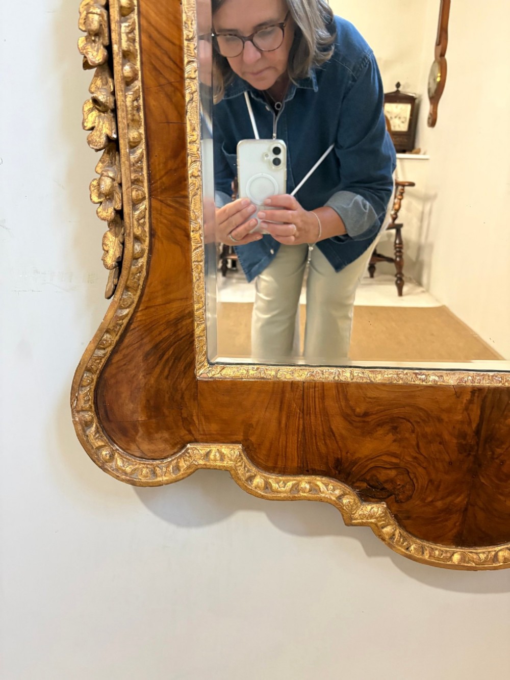 An eighteenth-century style wall mirror featuring a figured walnut veneer frame, carved giltwood foliate borders, a top cartouche cresting, and bevelled glass. View IV