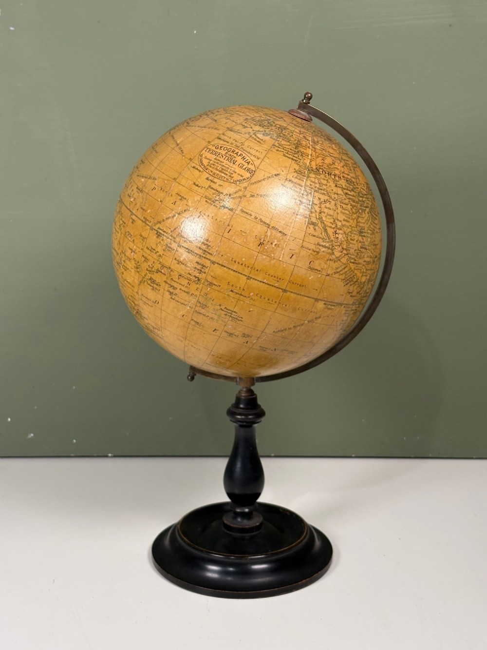 An antique terrestrial table globe with printed paper map gores, a brass semi-meridian arc, and a turned ebonised wooden base. View II