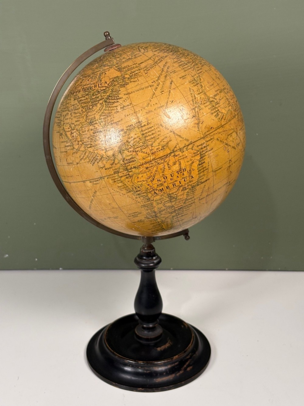 An antique terrestrial table globe with printed paper map gores, a brass semi-meridian arc, and a turned ebonised wooden base.