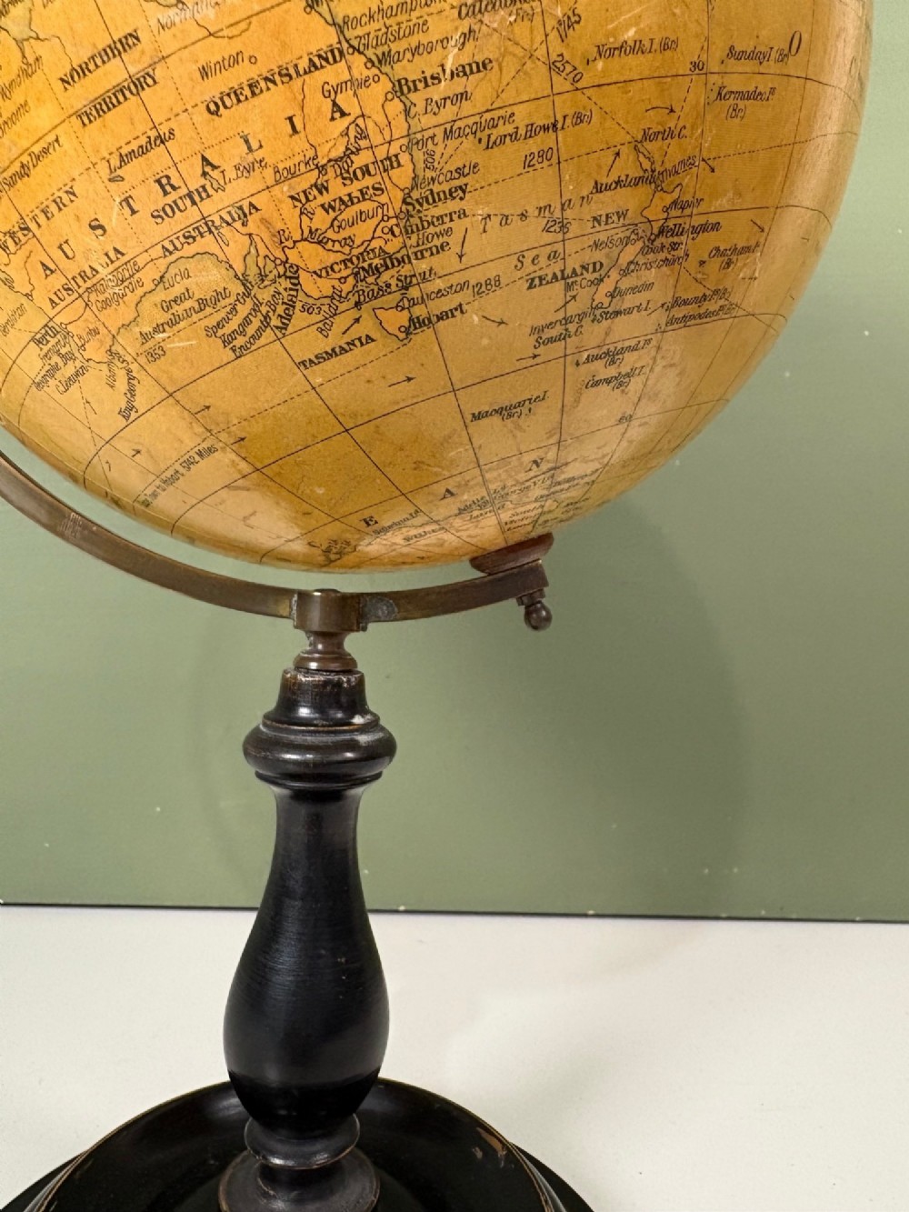 An antique terrestrial table globe with printed paper map gores, a brass semi-meridian arc, and a turned ebonised wooden base. View VII