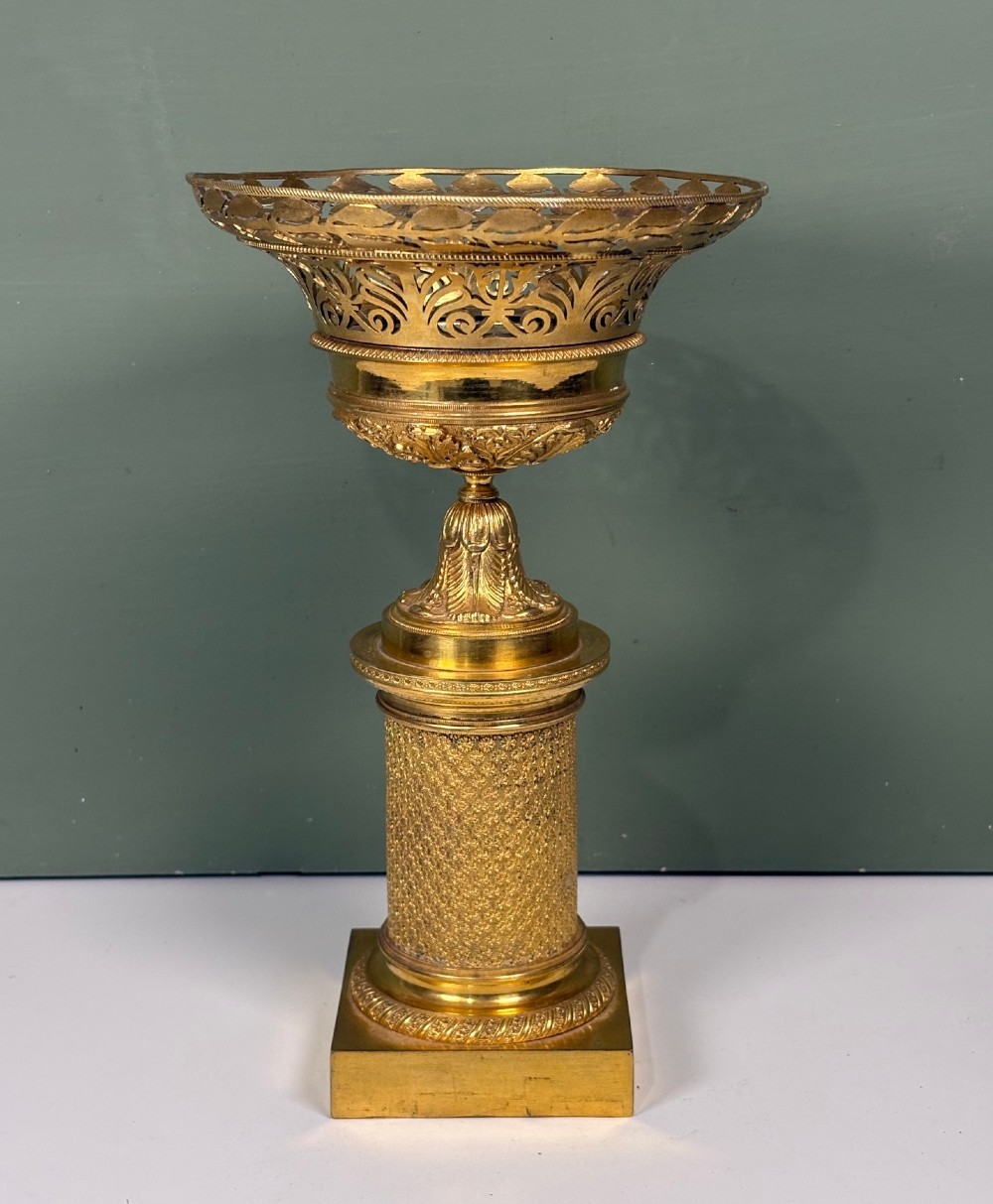 An early 19th-century gilt bronze ormolu vase featuring a pierced filigree flared rim, leaf-moulded bowl, textured pedestal column, and square base.