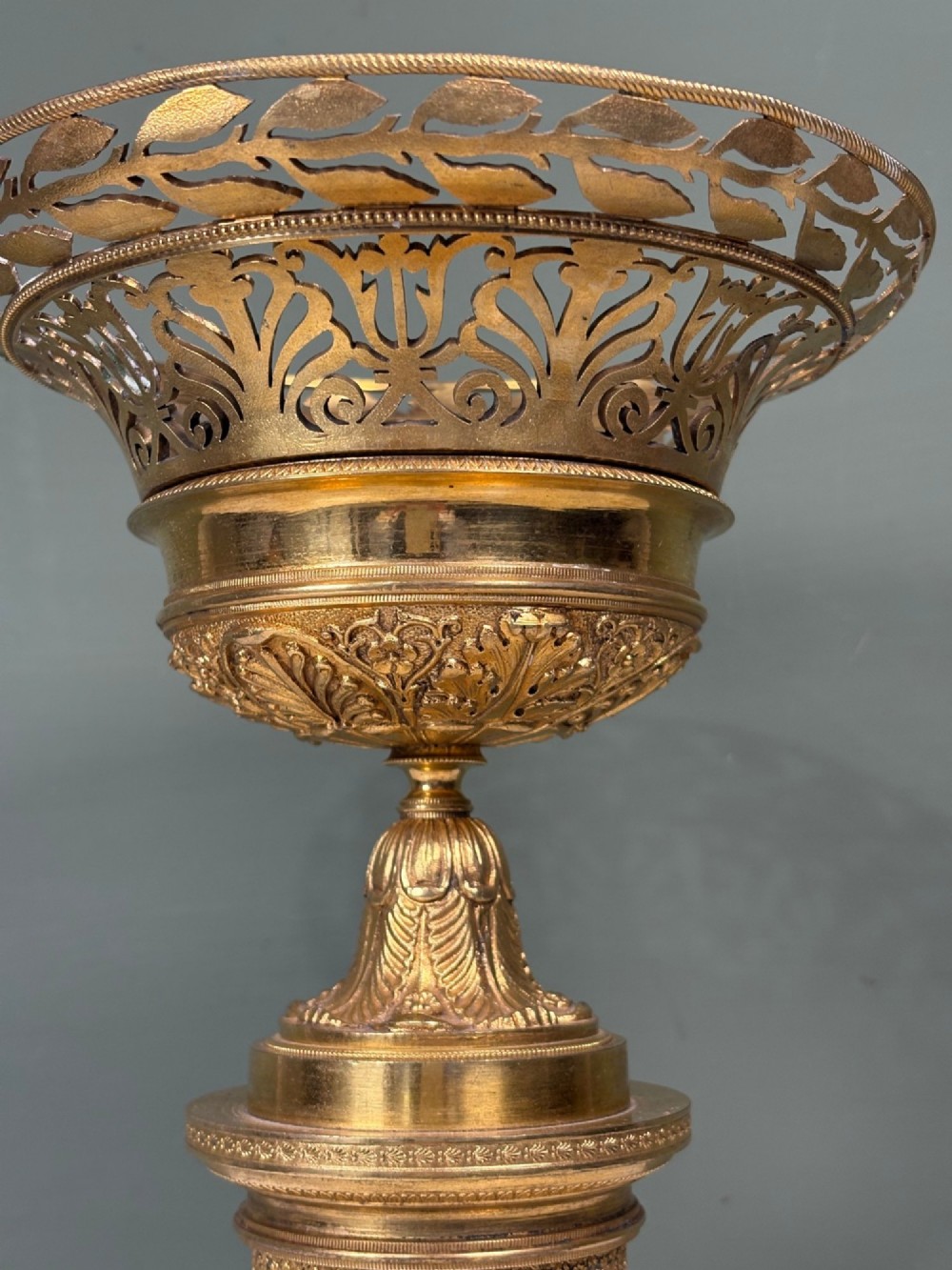 An early 19th-century gilt bronze ormolu vase featuring a pierced filigree flared rim, leaf-moulded bowl, textured pedestal column, and square base. View V
