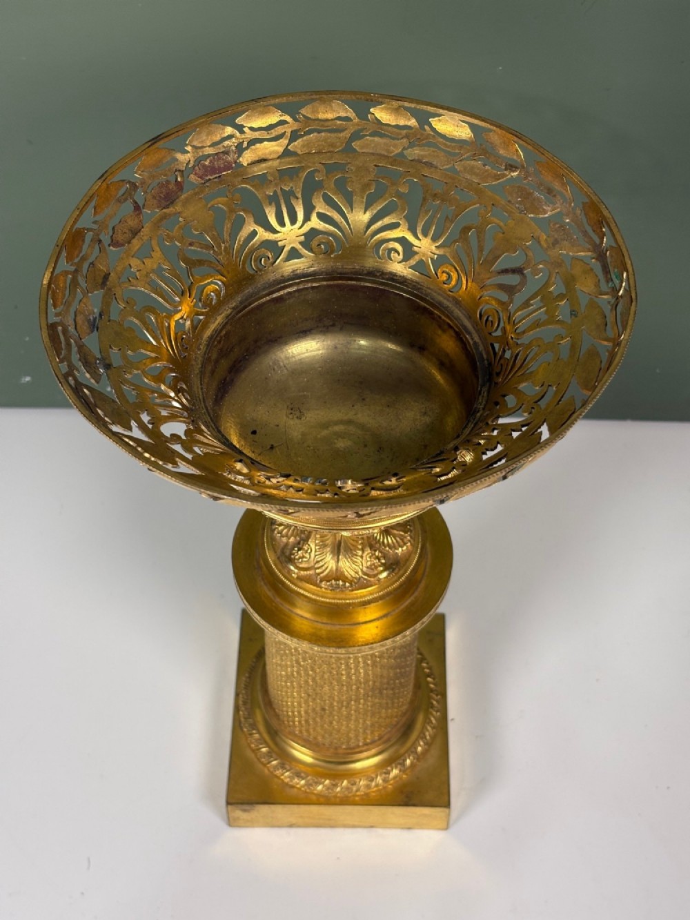 An early 19th-century gilt bronze ormolu vase featuring a pierced filigree flared rim, leaf-moulded bowl, textured pedestal column, and square base. View VI
