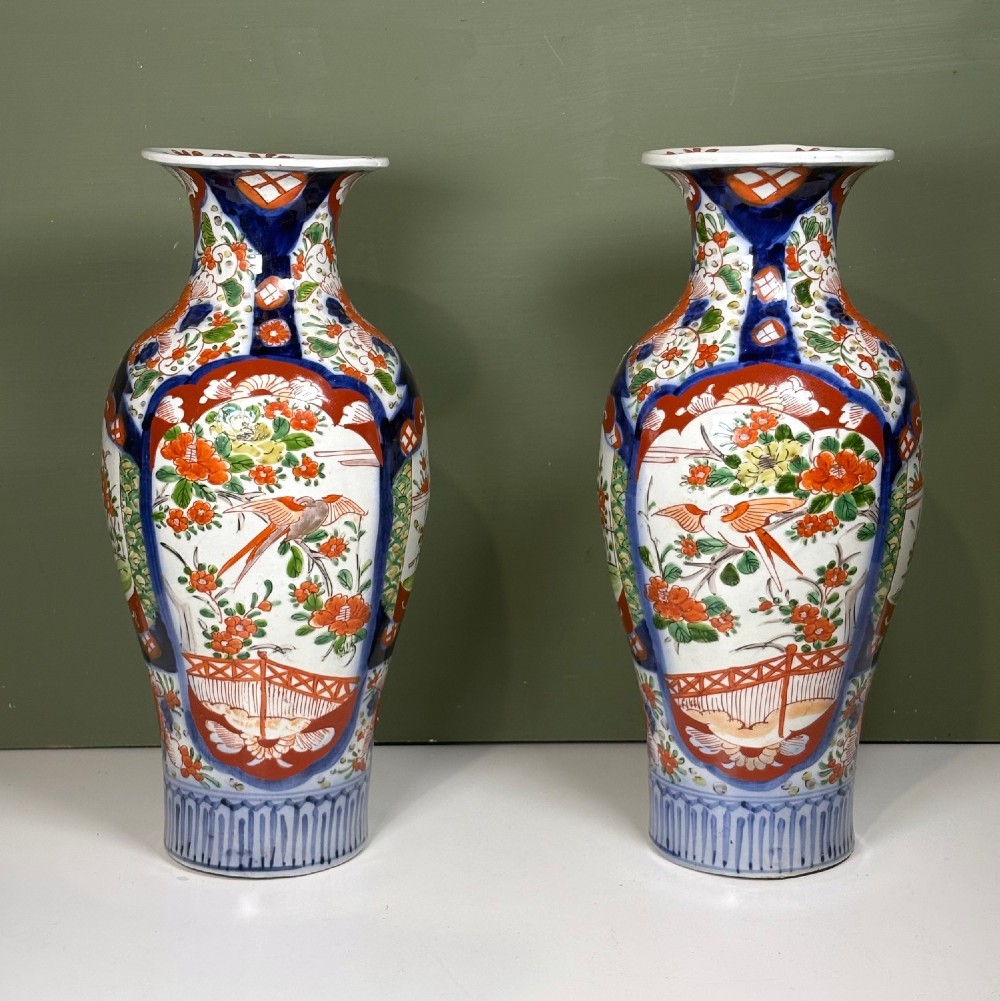 A matching pair of nineteenth-century Japanese Imari porcelain vases featuring hand-painted floral panels, bird motifs, and intricate cobalt blue and iron-red geometric patterns.