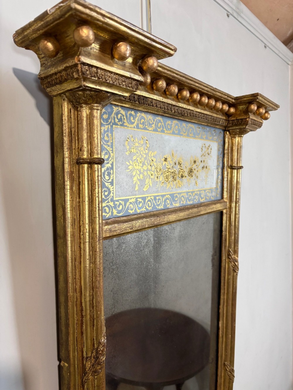 A vertical Regency giltwood pier mirror with fluted side columns, ball-ornamented cornice, and a decorative floral verre eglomise glass panel. View IV