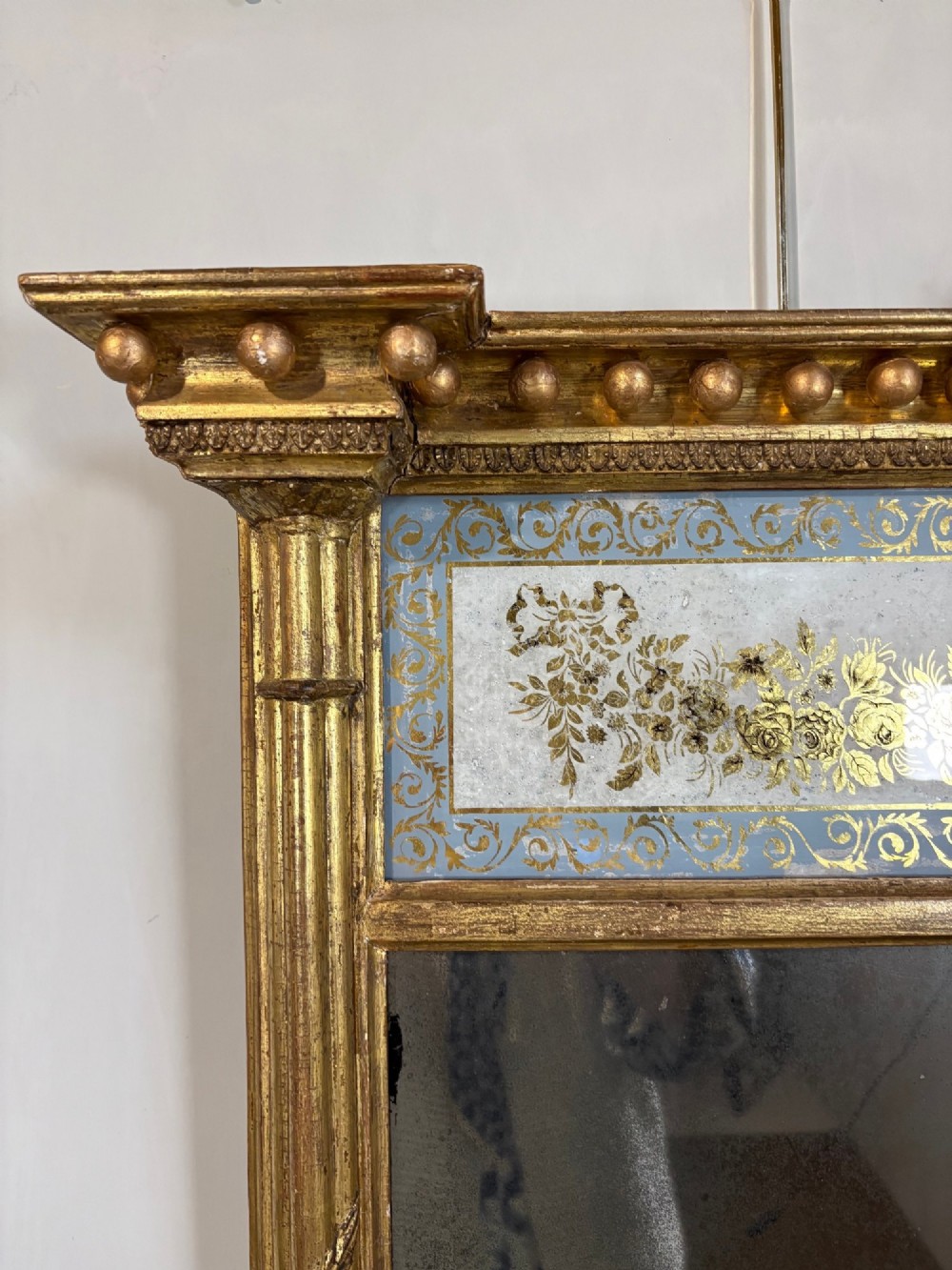 A vertical Regency giltwood pier mirror with fluted side columns, ball-ornamented cornice, and a decorative floral verre eglomise glass panel. View VII