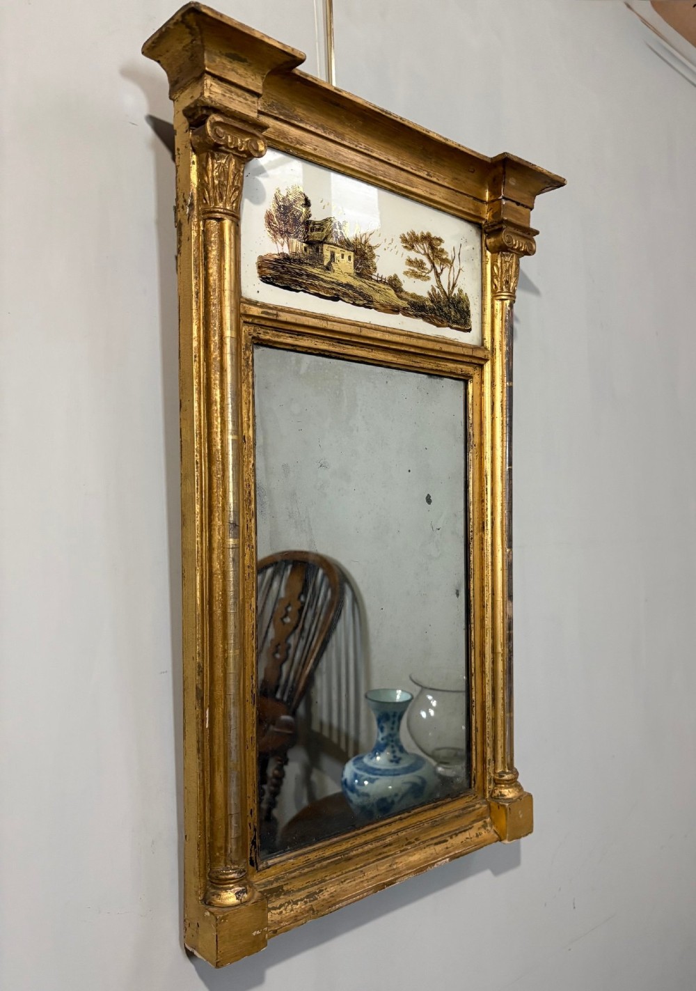 A Regency period giltwood pier glass mirror featuring fluted side columns, a stepped pediment cornice, and an upper verre eglomise glass panel depicting a rural building and landscape. View II
