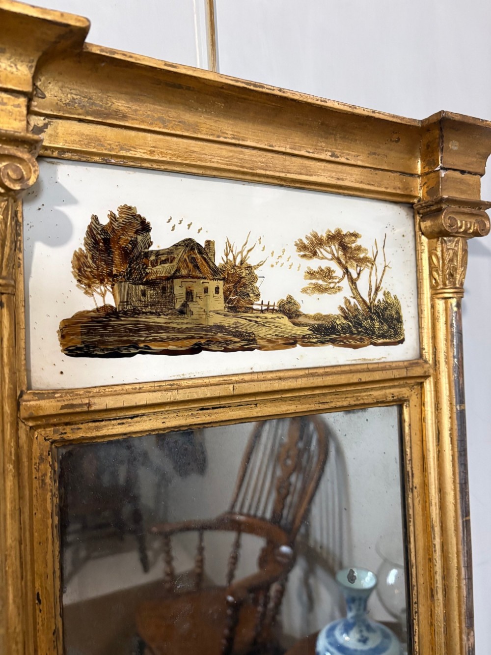 A Regency period giltwood pier glass mirror featuring fluted side columns, a stepped pediment cornice, and an upper verre eglomise glass panel depicting a rural building and landscape. View III