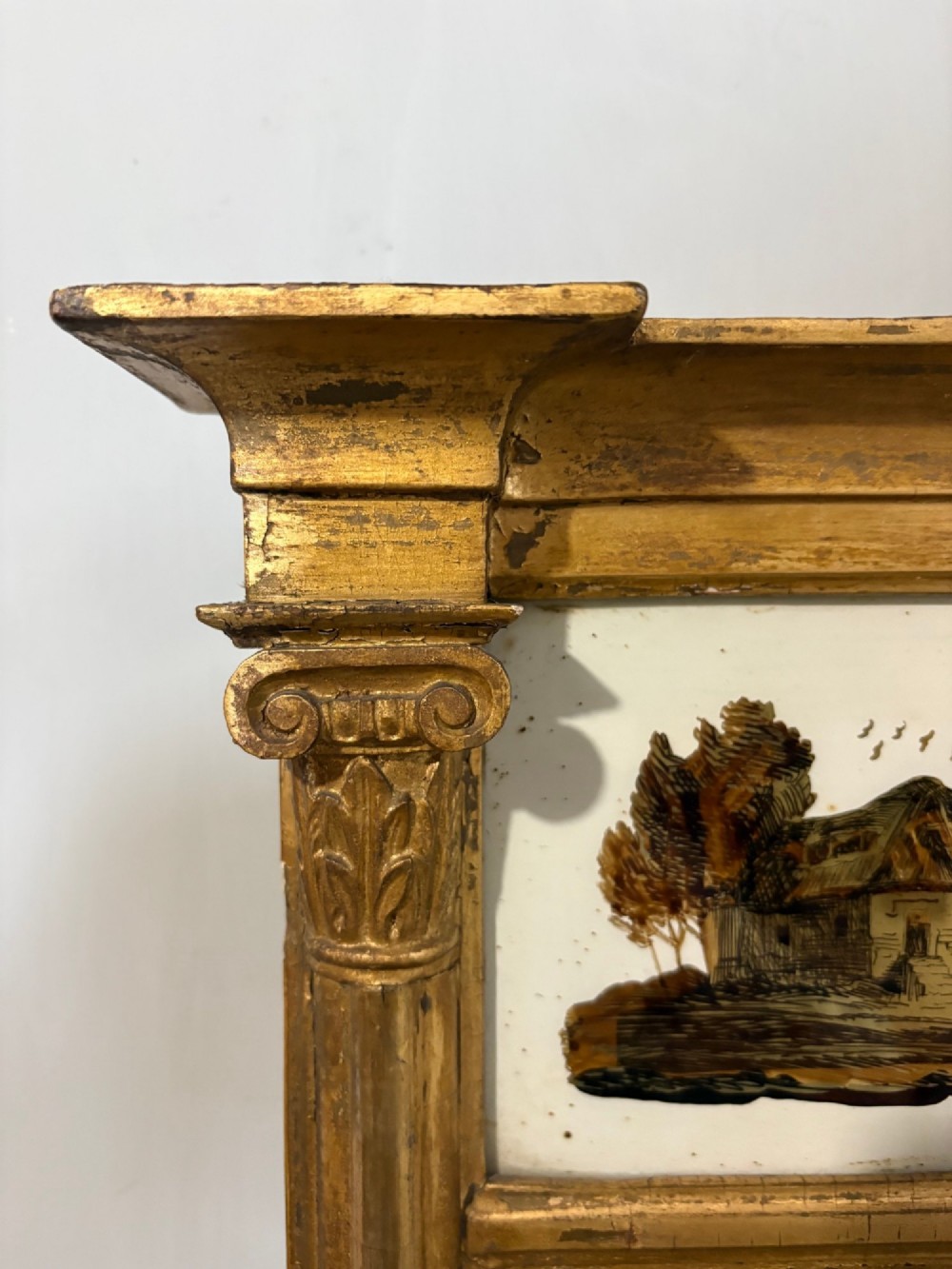 A Regency period giltwood pier glass mirror featuring fluted side columns, a stepped pediment cornice, and an upper verre eglomise glass panel depicting a rural building and landscape. View V