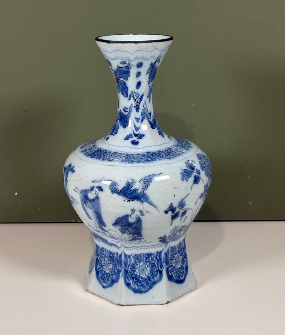 An 18th-century octagonal Delftware vase featuring hand-painted cobalt blue Chinoiserie figures and floral patterns against a white glaze.