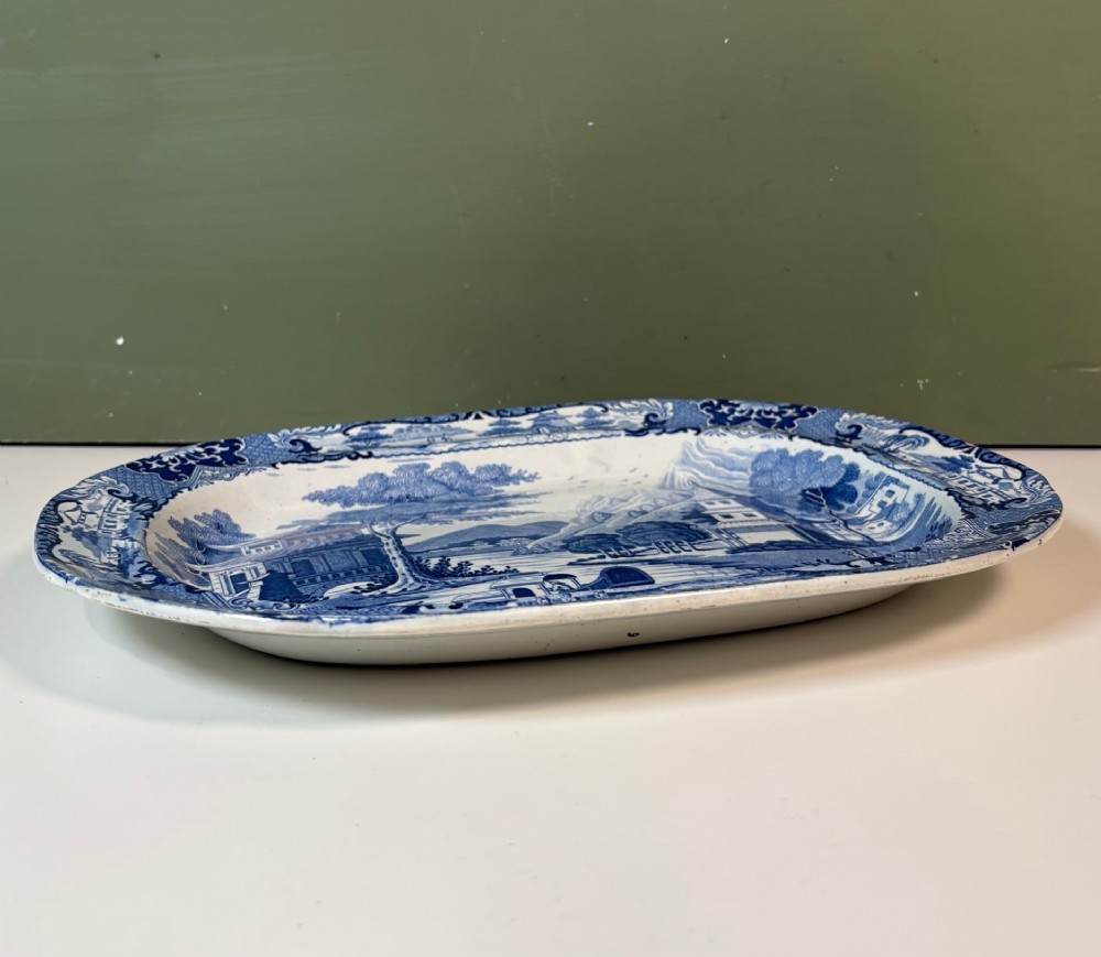 A 19th-century oval blue and white earthenware platter featuring a printed Chinoiserie landscape scene with pagodas, a river boat, and decorative scrollwork borders. View VI