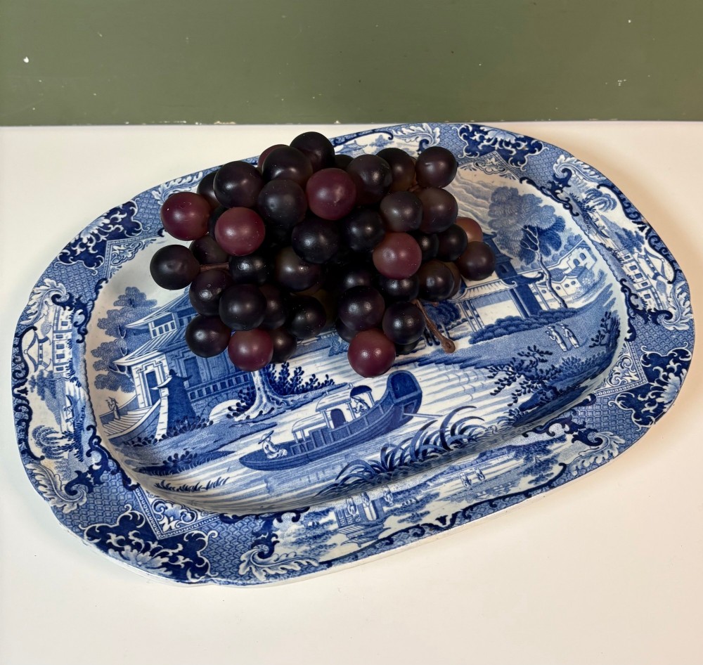 A 19th-century oval blue and white earthenware platter featuring a printed Chinoiserie landscape scene with pagodas, a river boat, and decorative scrollwork borders. View VII