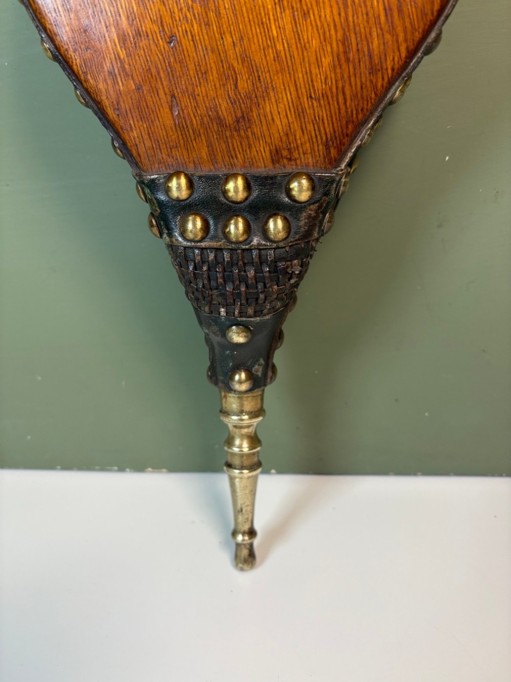 A nineteenth-century oak fire bellows with dark leather trim, brass studding, a leather hanging loop, and a turned brass nozzle. View II