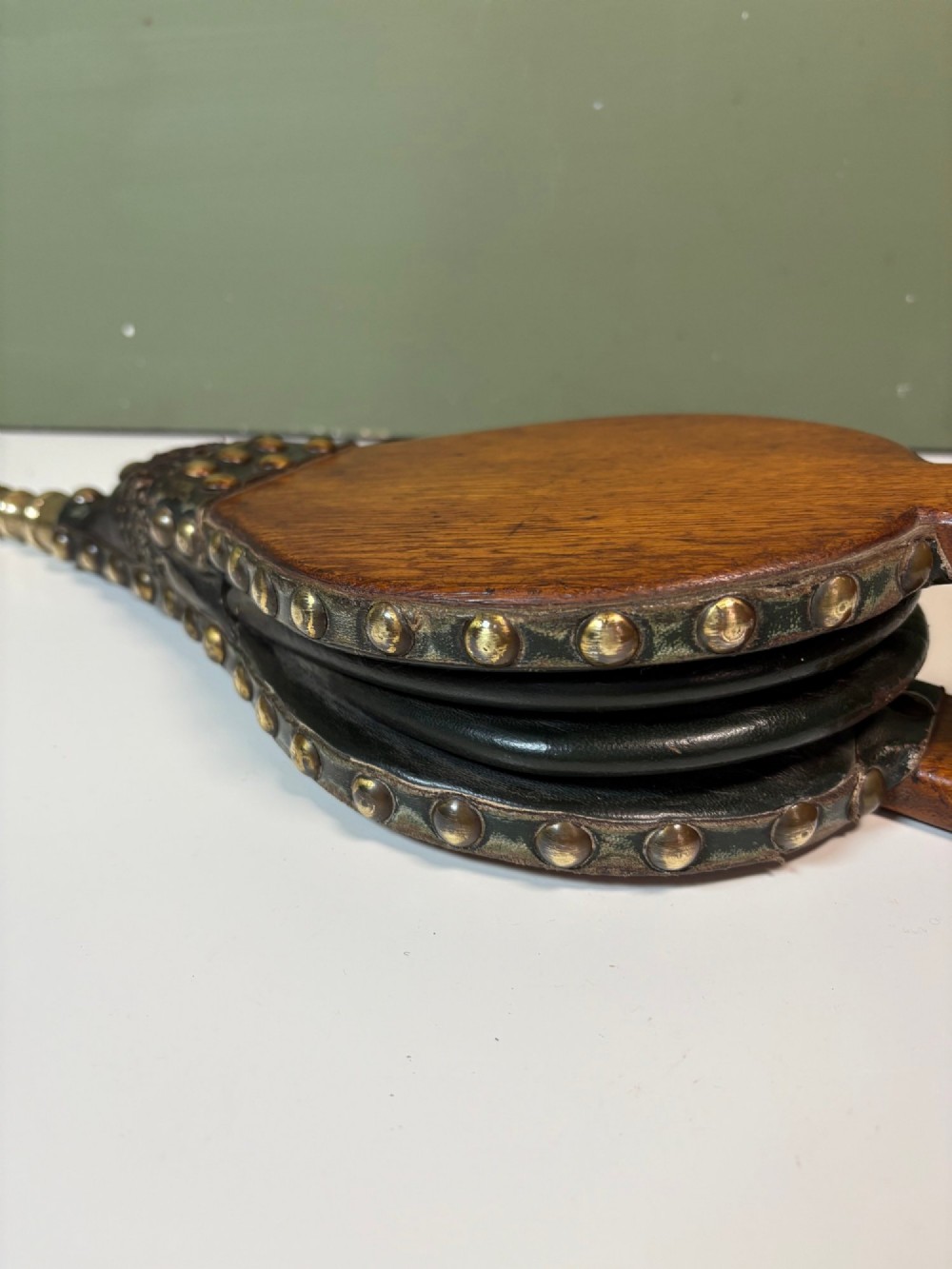 A nineteenth-century oak fire bellows with dark leather trim, brass studding, a leather hanging loop, and a turned brass nozzle. View V