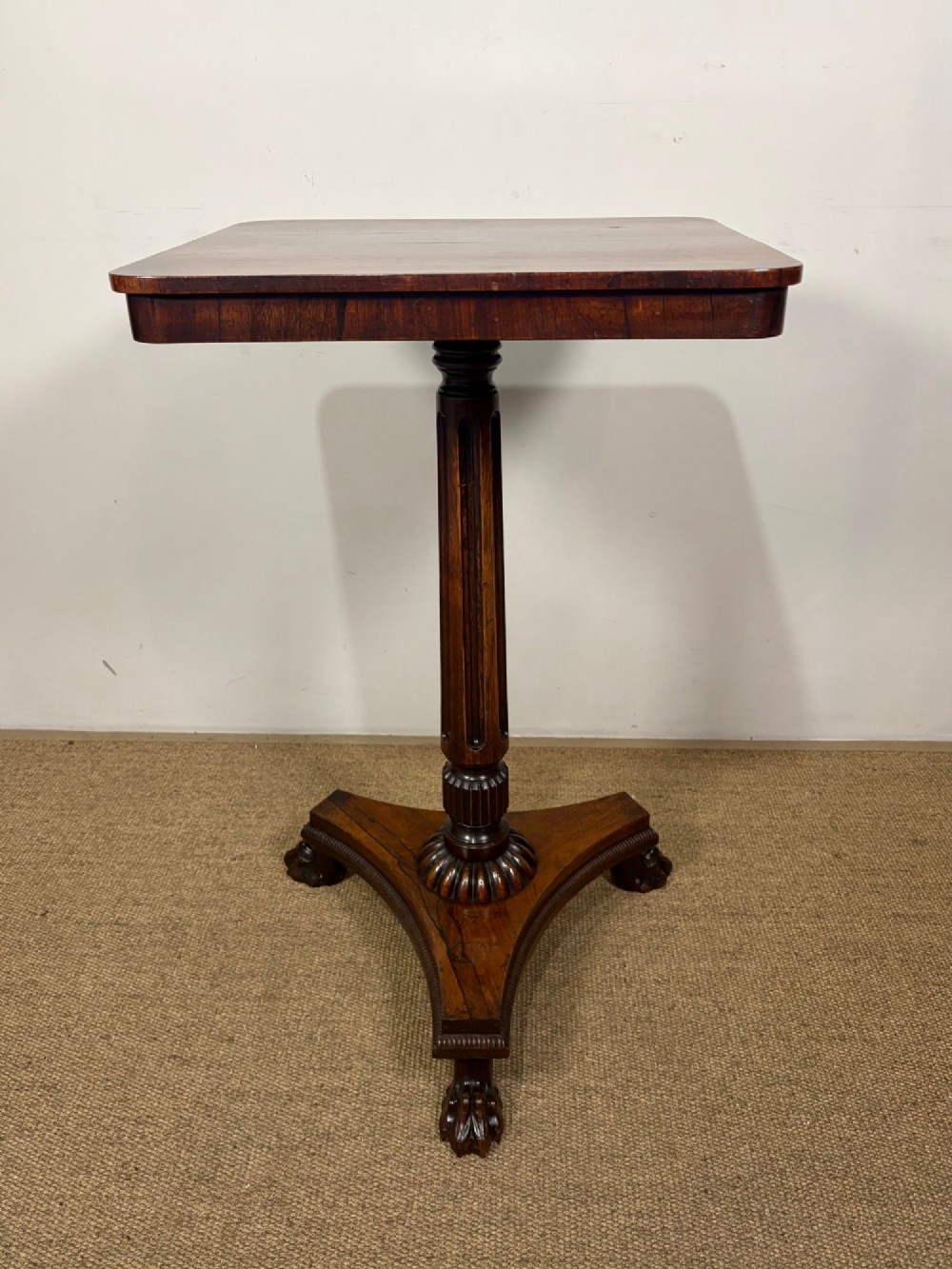 A nineteenth-century rosewood pedestal table featuring a square top, fluted central column, triform base, and carved claw feet.