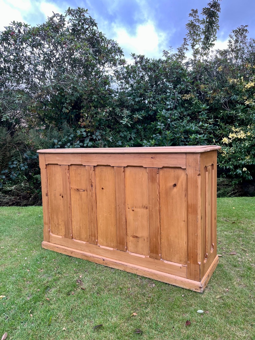 A rectangular antique pine log box featuring vertical timber panelling, a flat top surface, and a solid plinth base.