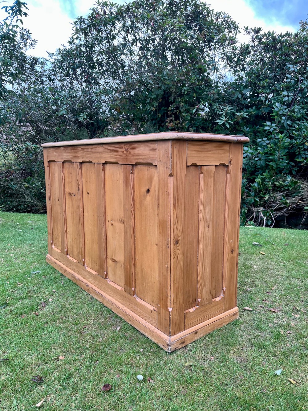 A rectangular antique pine log box featuring vertical timber panelling, a flat top surface, and a solid plinth base. View IX