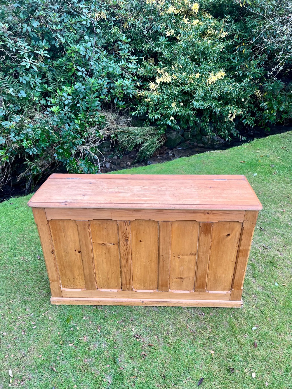 A rectangular antique pine log box featuring vertical timber panelling, a flat top surface, and a solid plinth base. View XIV