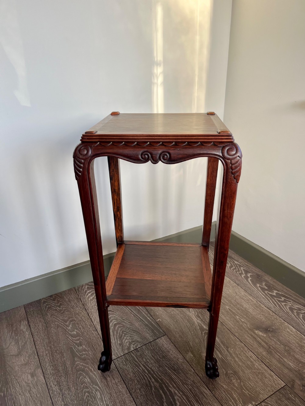 A tall, square antique rosewood lamp table featuring carved aprons, a lower shelf tier, and slender legs ending in carved feet.