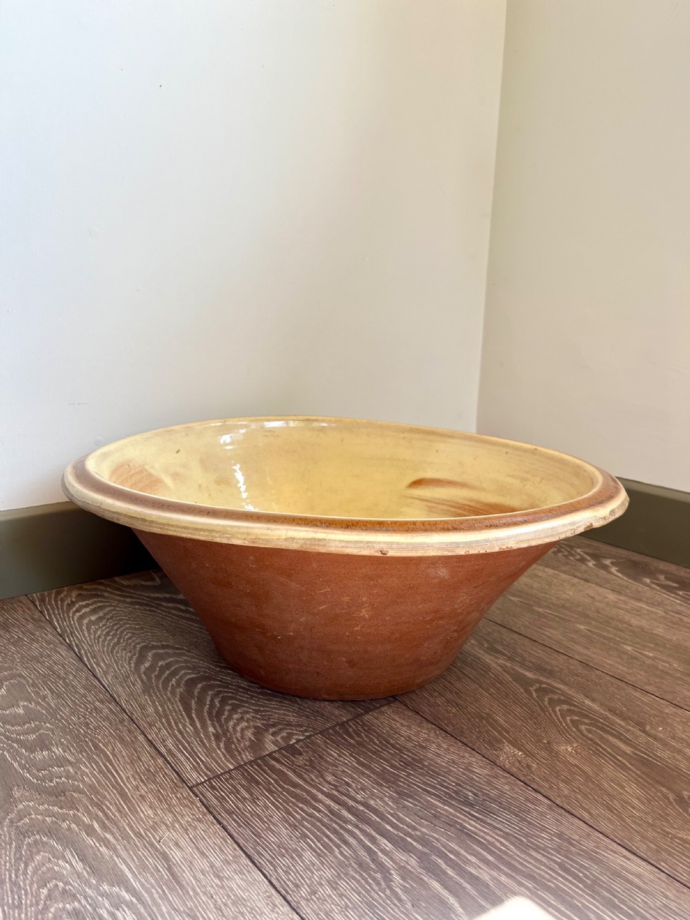 A large flared antique terracotta dairy bowl featuring a pale yellow glazed interior and a rounded rolled rim.