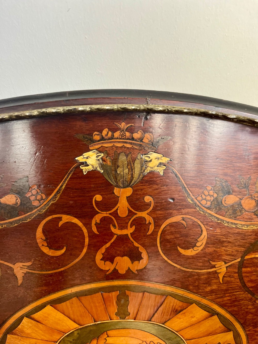 An oval wooden Edwardian serving tray featuring detailed marquetry inlay of scrollwork and cherubs with two brass side handles and a metal rim. View II