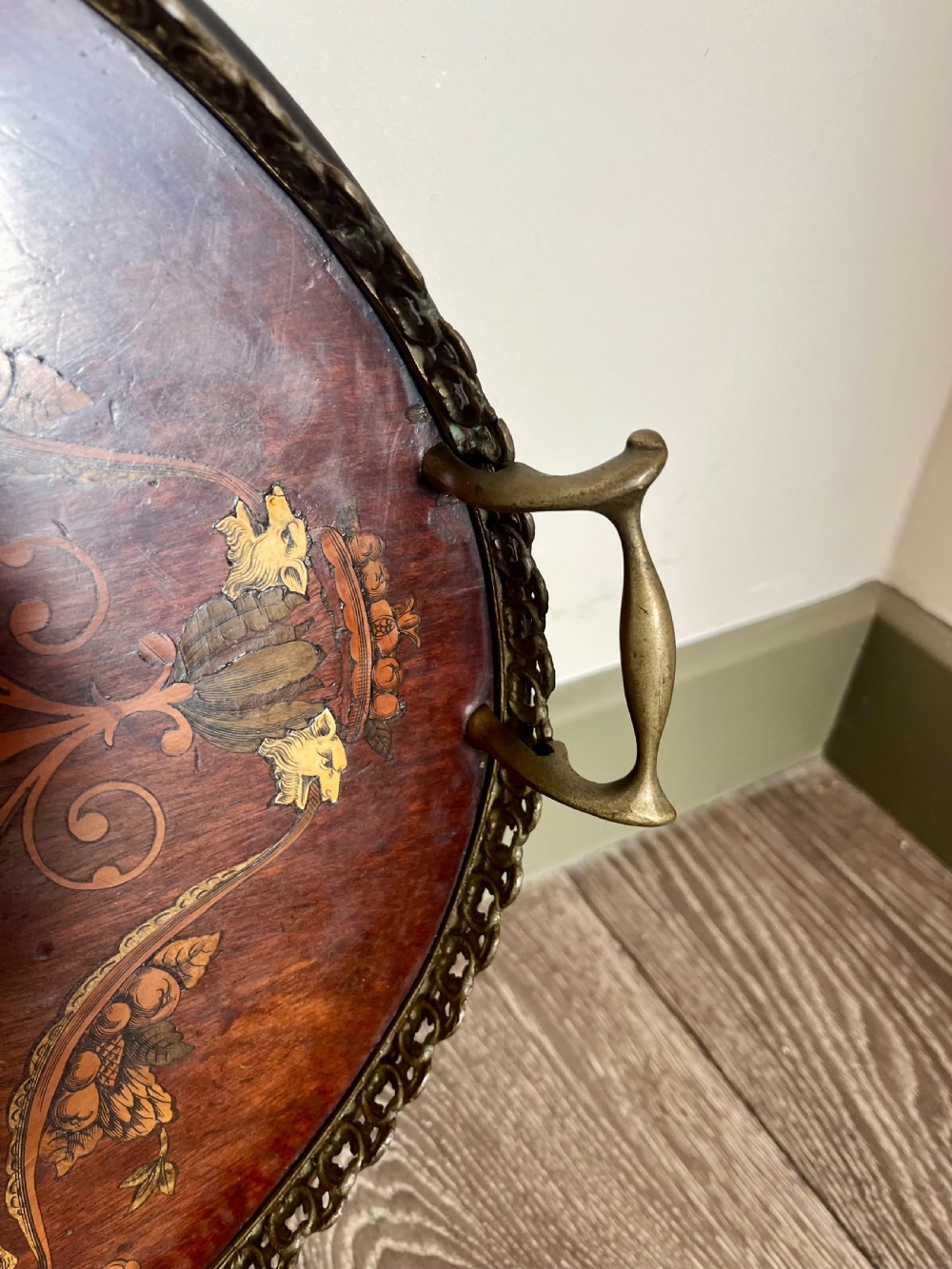 An oval wooden Edwardian serving tray featuring detailed marquetry inlay of scrollwork and cherubs with two brass side handles and a metal rim. View V