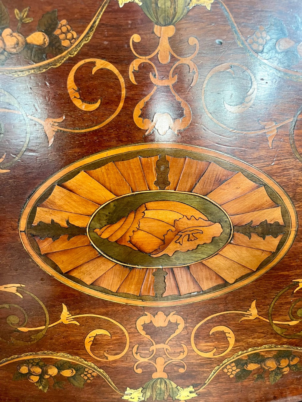 An oval wooden Edwardian serving tray featuring detailed marquetry inlay of scrollwork and cherubs with two brass side handles and a metal rim. View VI