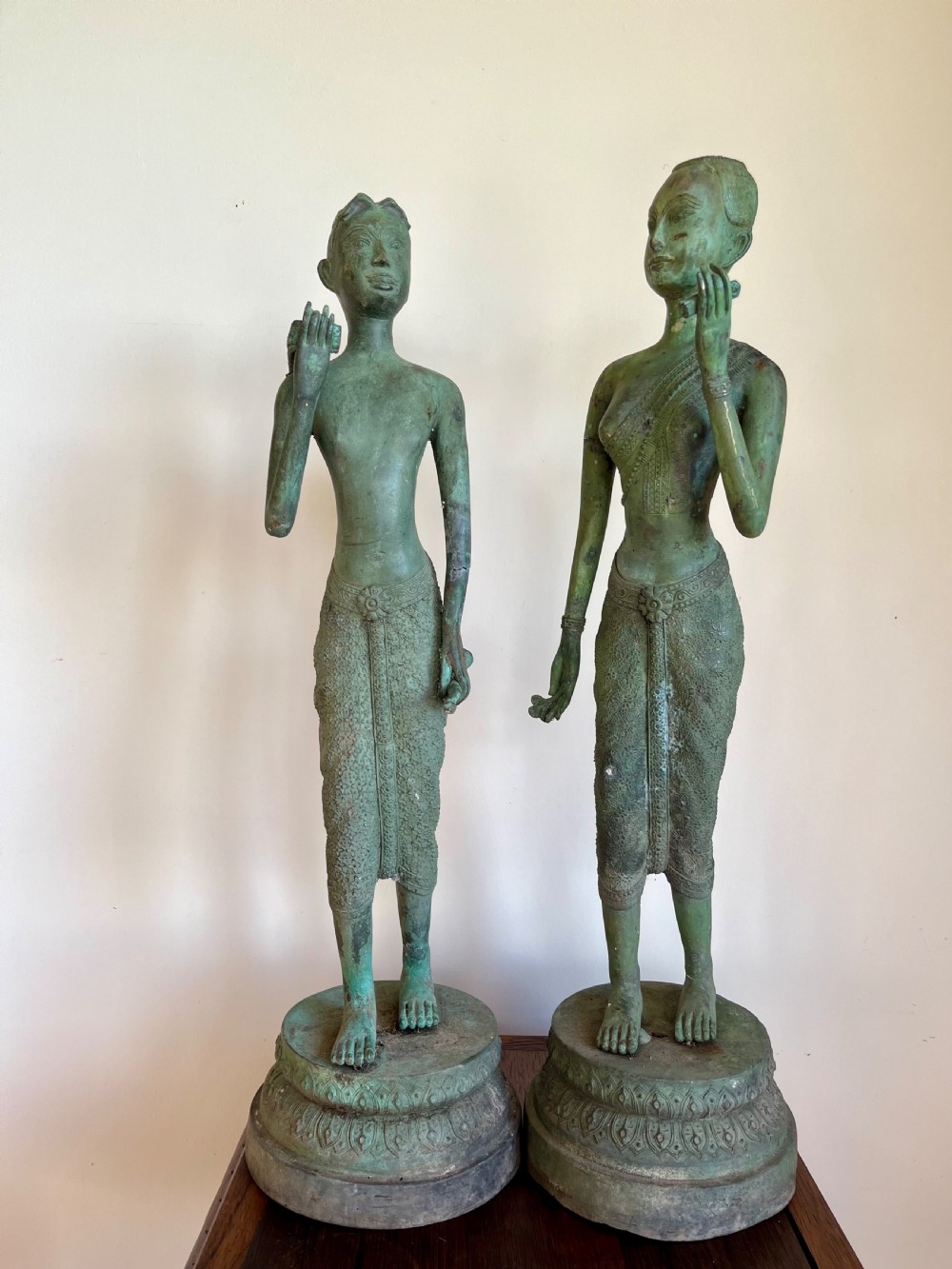 A pair of full-length bronze statues depicting a standing male and female figure with a green verdigris patina, positioned on rounded carved bases.